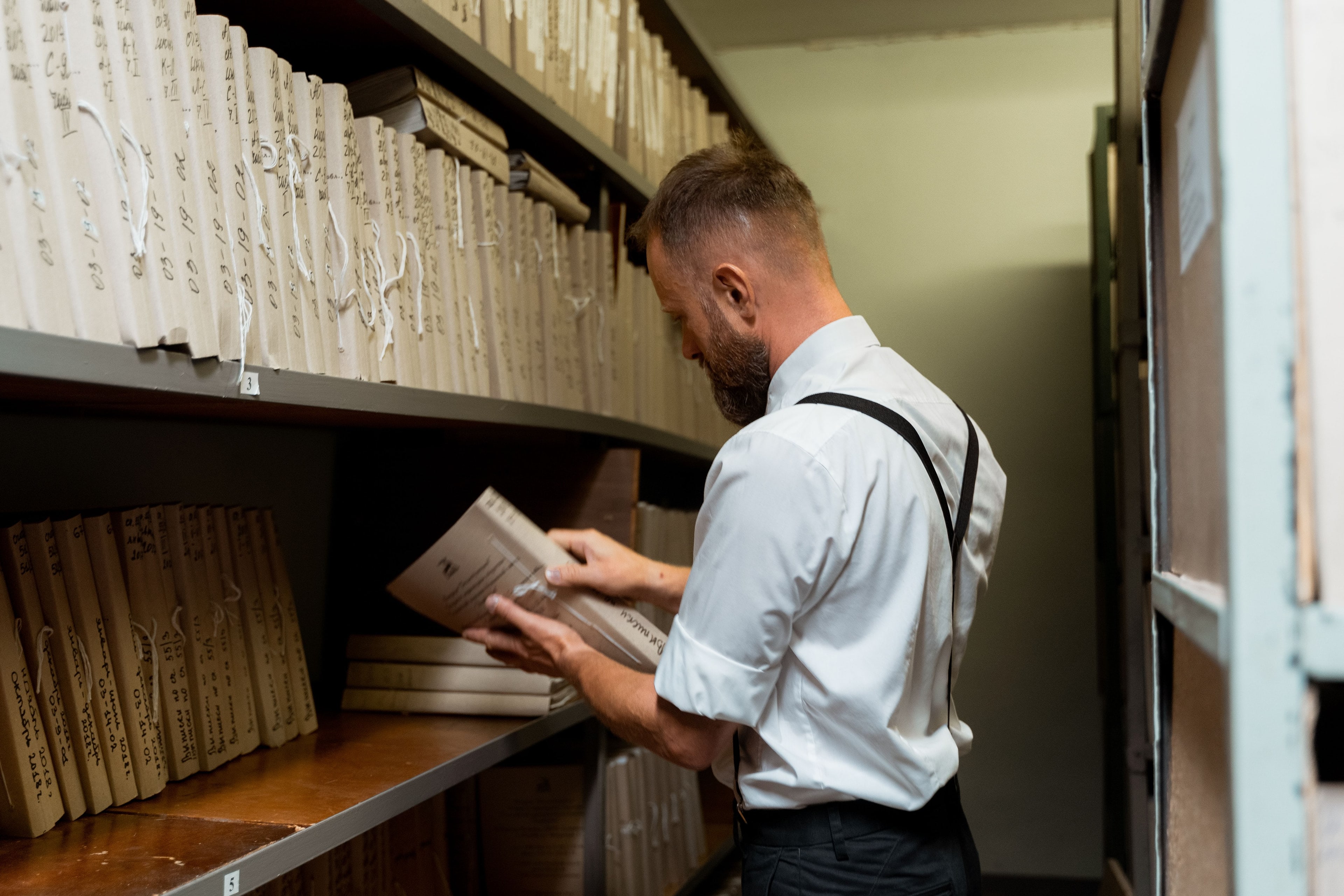 Un homme consulte un dossier tiré d'une étagère d'archives.