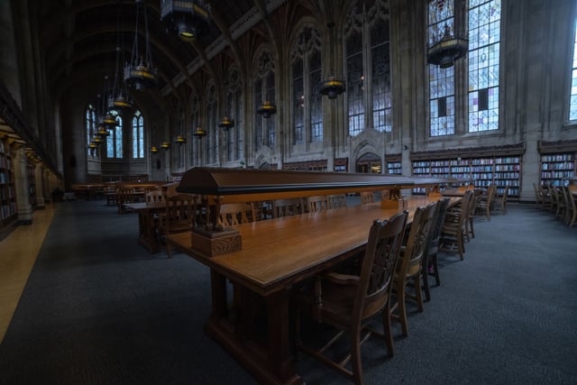 Grande salle de lecture ancienne, longues tables de bois et vitraux, sans personne.