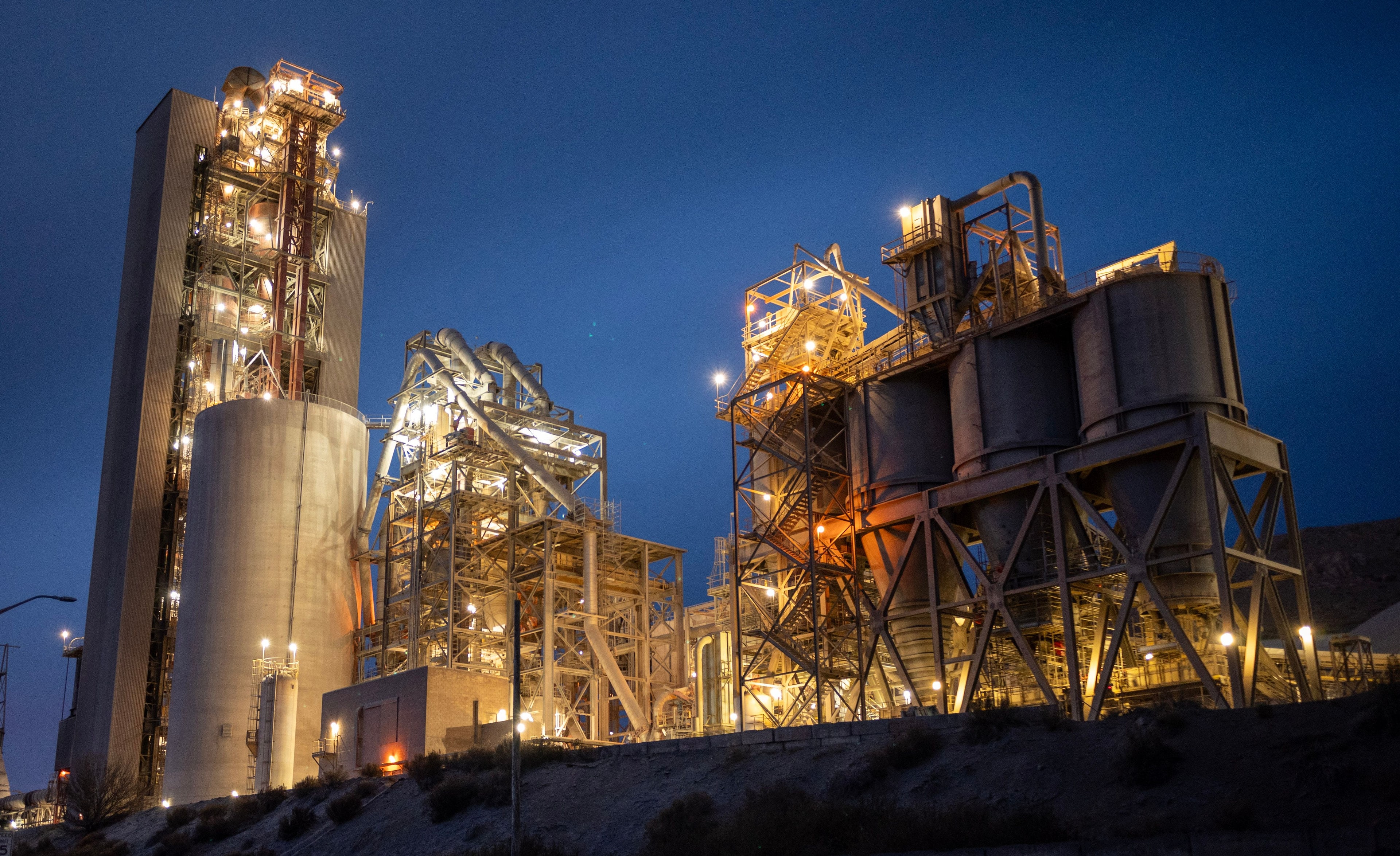Site industriel de nuit, silos et passerelles éclairés sous un ciel bleu profond.