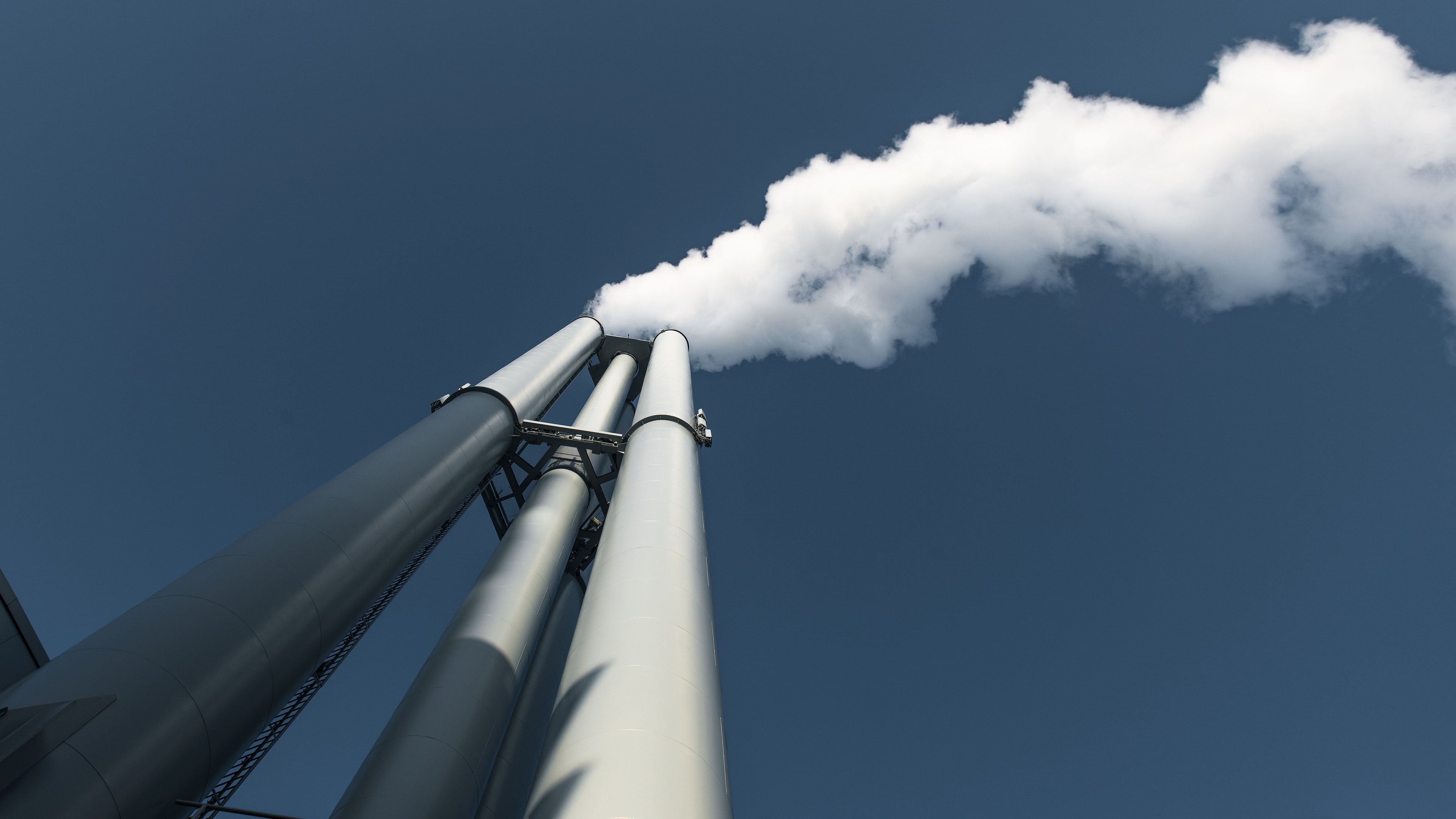 Cheminées industrielles et panache de vapeur sur un ciel bleu.
