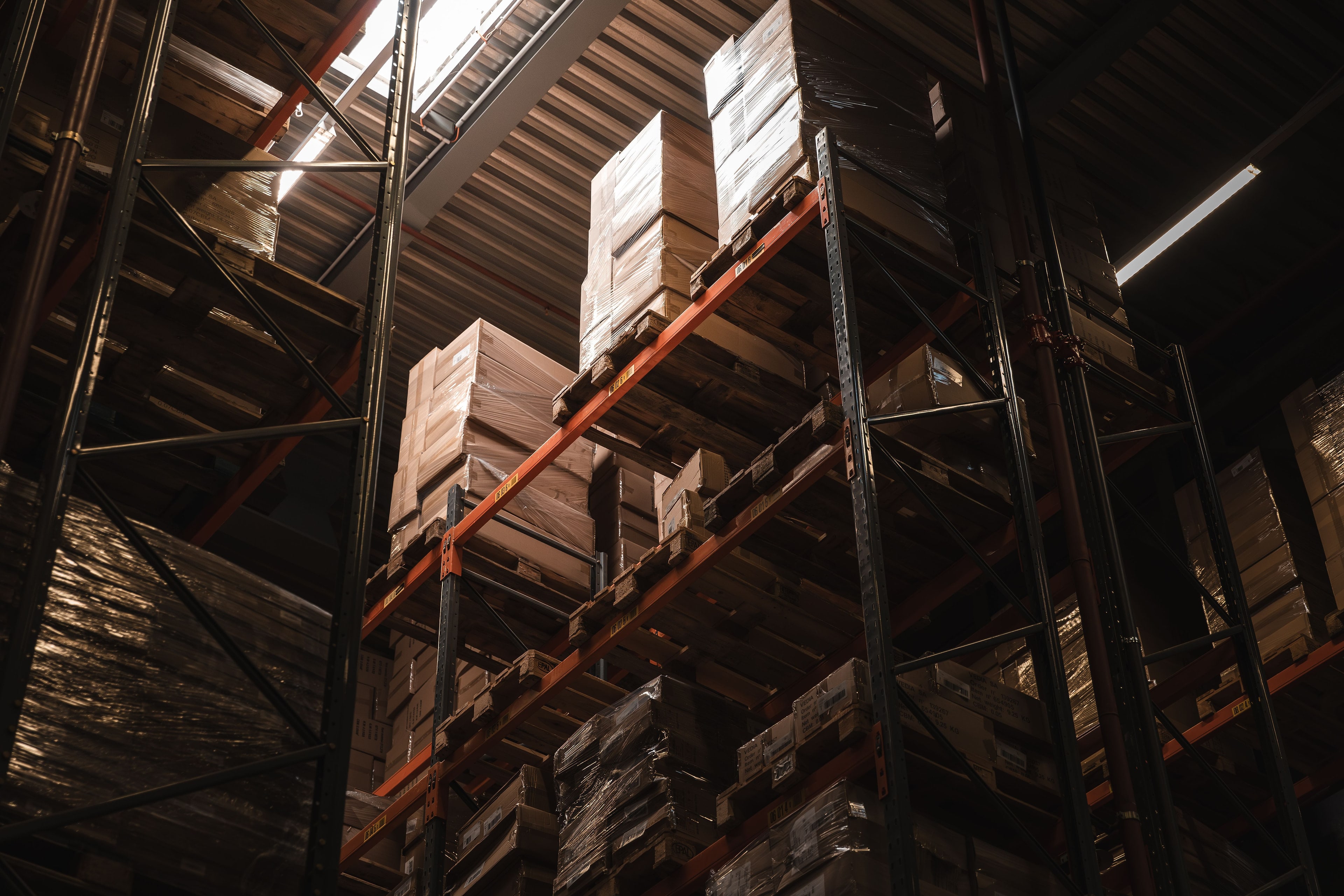 Rayonnages d'entrepôt chargés de cartons, vus d'en bas dans une lumière chaude.