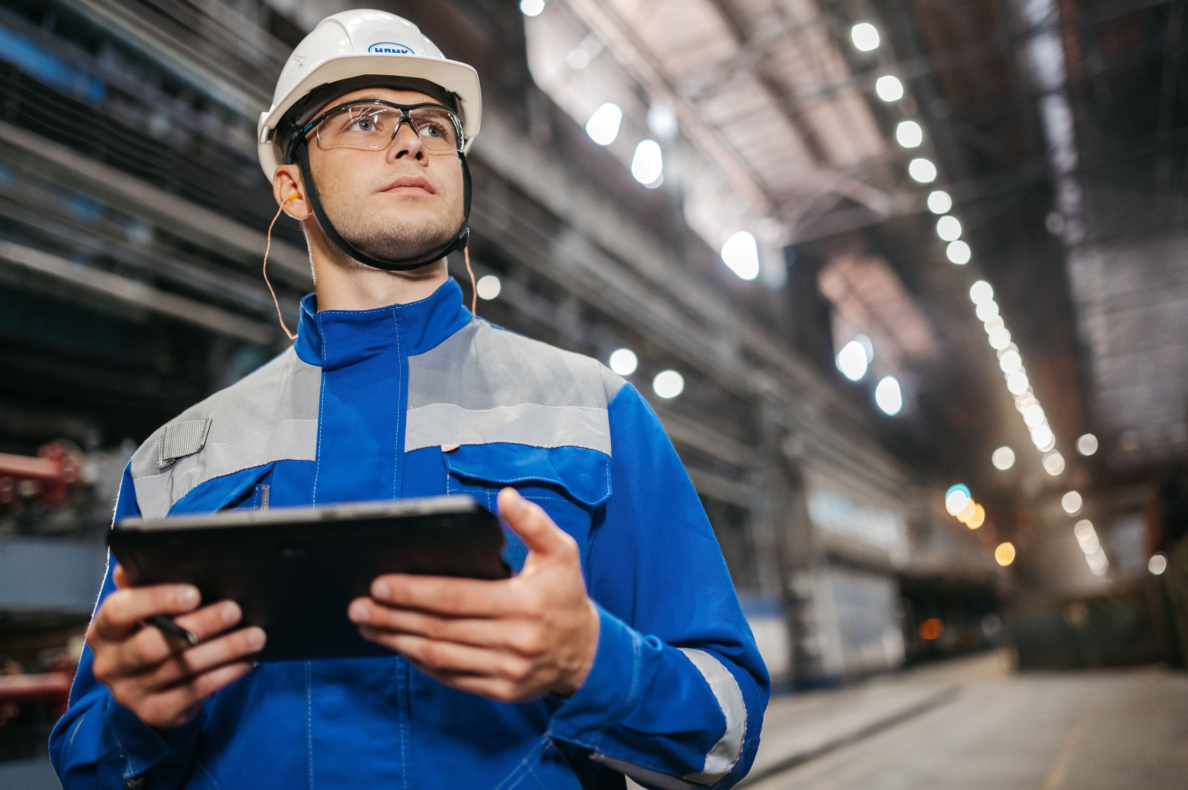 Technicien en casque, une tablette à la main, dans un atelier industriel.